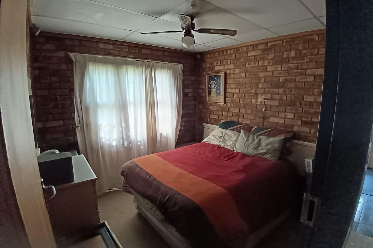 A bedroom featuring exposed brick walls, a ceiling fan, and a window with curtains, presenting a dated aesthetic.