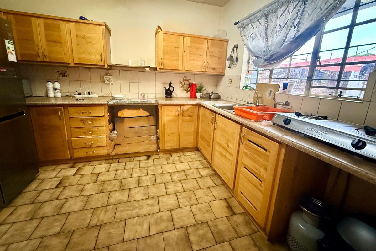 A functional kitchen featuring wooden cabinetry, tiled flooring, and a window overlooking the exterior, offering a practical layout for daily meal preparation.
