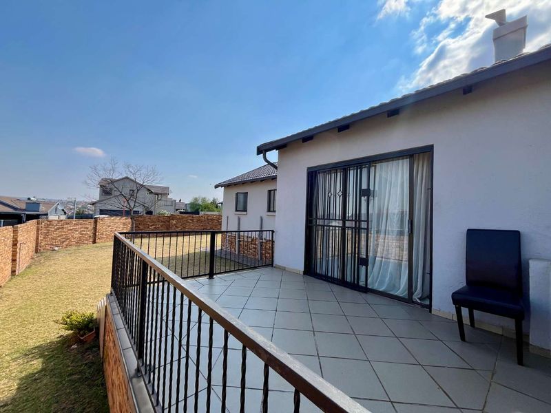 An elevated patio featuring tiled flooring and a metal balustrade, providing access to the garden area through a sliding glass door.