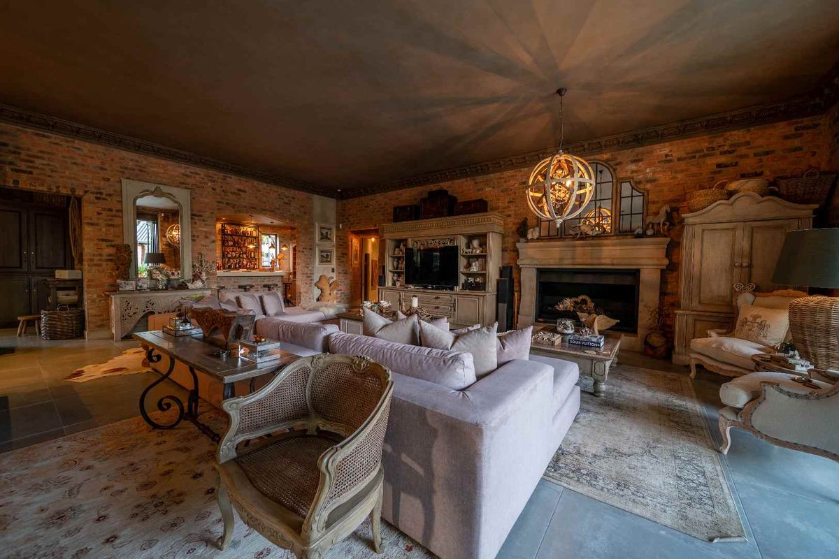Spacious living room featuring exposed brick walls, a large stone fireplace, and decorative crown molding, creating a warm and character-filled atmosphere.