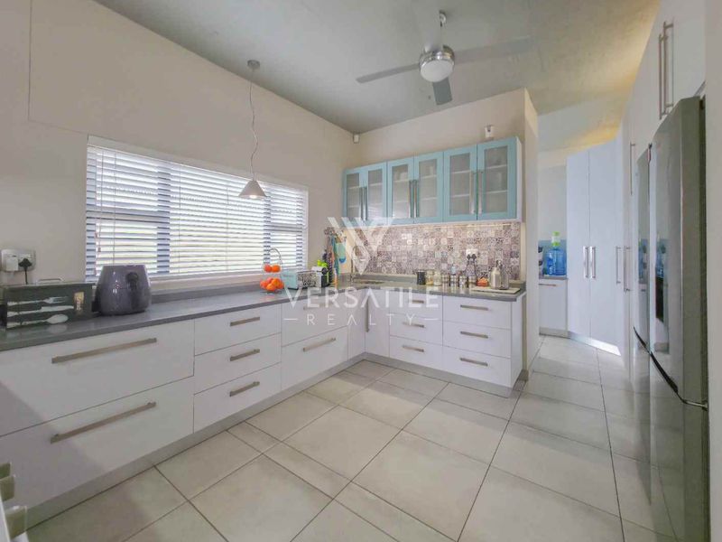 Modern kitchen featuring white cabinetry, light blue glass-front upper cabinets, patterned tile backsplash, stone countertops, and neutral floor tiles.