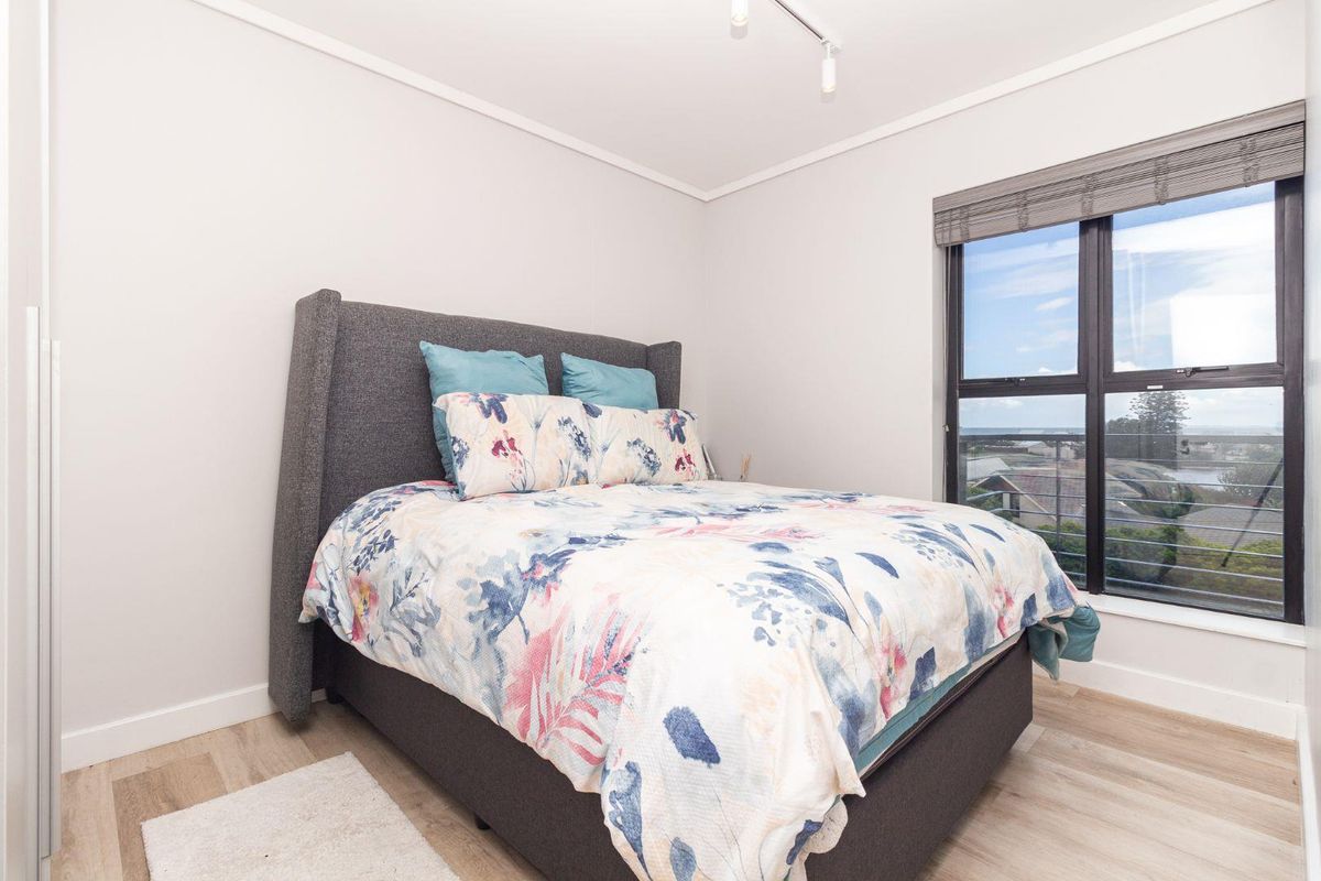 A bright bedroom featuring light laminate flooring, a built-in wardrobe, and a large window offering natural light and exterior views.