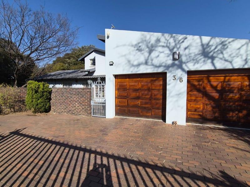 Front exterior view featuring a double garage with wooden doors, a brick paved driveway, and a secure brick boundary wall with a pedestrian gate.