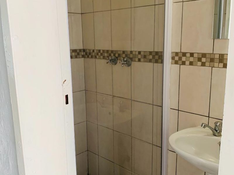 A functional bathroom featuring a shower enclosure with tiled walls and a pedestal basin.