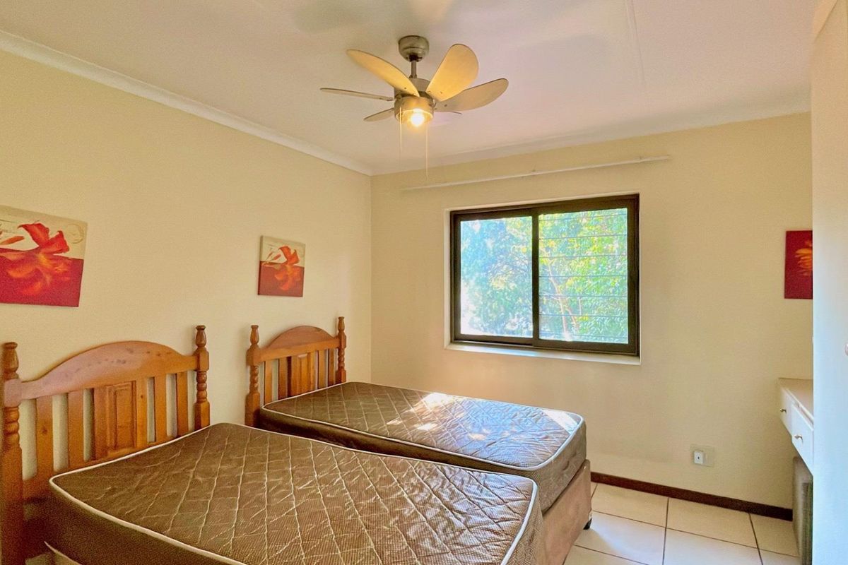 A bedroom featuring tiled flooring, a ceiling fan, and a window with security bars, providing a functional and well-lit living space.