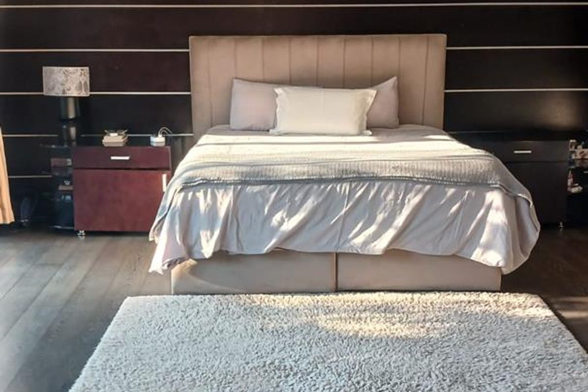 A spacious bedroom featuring dark wood flooring and a distinctive horizontal-paneled feature wall with recessed ceiling lighting.