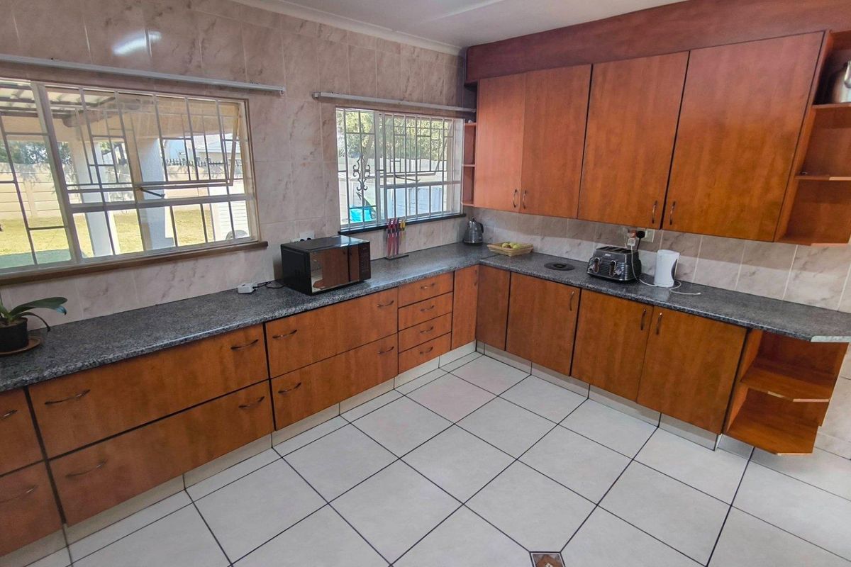A functional kitchen featuring wood-finish cabinetry, granite countertops, tiled flooring, and large windows with security bars for natural light.