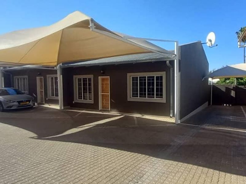 Front exterior view of the townhouse featuring a paved driveway and covered parking area with shade sails.