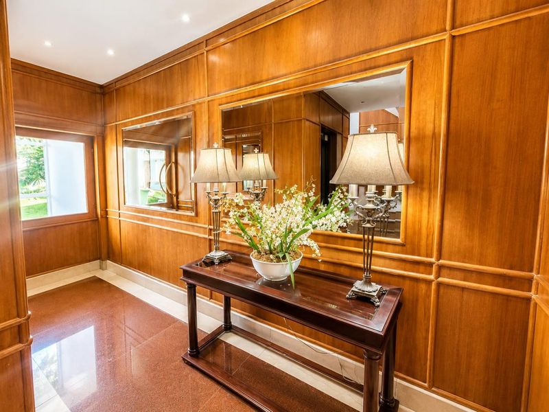 Elegant hallway featuring rich wood wall paneling, polished stone flooring, and integrated wall mirrors, creating a sophisticated and warm entrance space.
