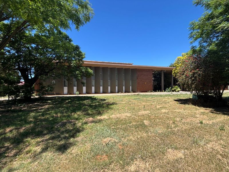 Front view of a commercial office building featuring a brick facade, vertical window panels, and a flat roof, set within a spacious lawn area.