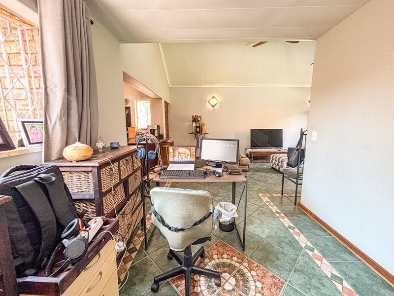 Open-plan living area featuring vaulted ceilings, ceiling fan, and decorative tiled flooring, providing a versatile space for a home office and lounge setup.