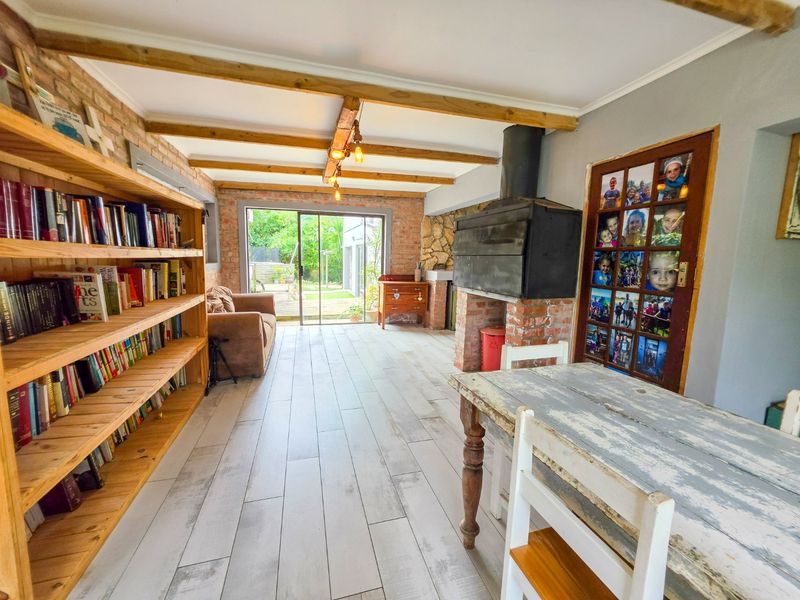 Spacious living area featuring exposed brick walls, timber ceiling beams, a built-in fireplace, and sliding doors providing direct access to the garden.