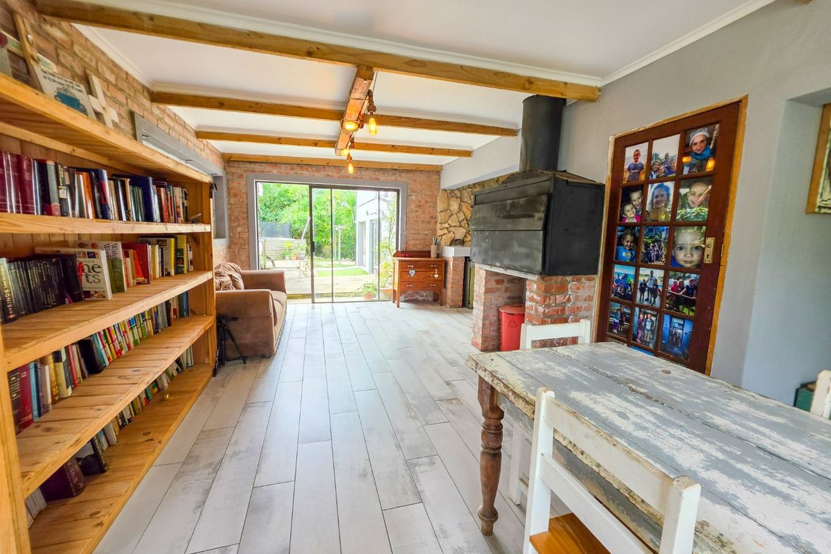 Spacious living area featuring exposed brick walls, timber ceiling beams, a built-in fireplace, and sliding doors providing direct access to the garden.