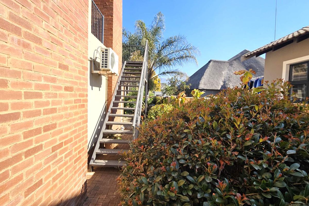 Rear exterior view of the property featuring a brick facade, paved walkway, and an external staircase leading to an upper level.