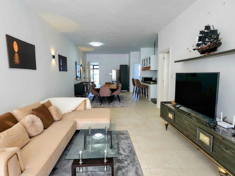 An open-plan living and dining area featuring tiled flooring, modern wall lighting, and a functional kitchen space with a breakfast bar.