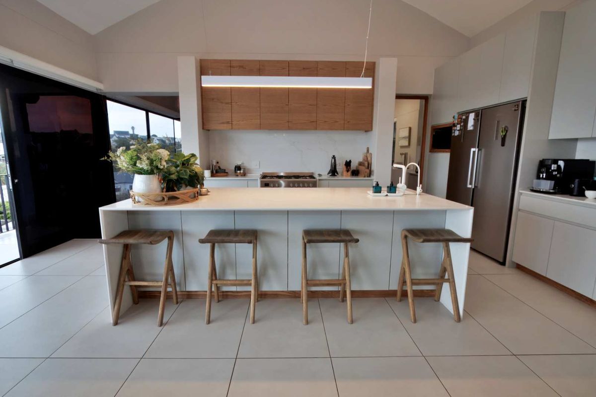 Modern open-plan kitchen featuring a large central island with stone countertop, sleek cabinetry, integrated appliances, and high-quality tiled flooring.