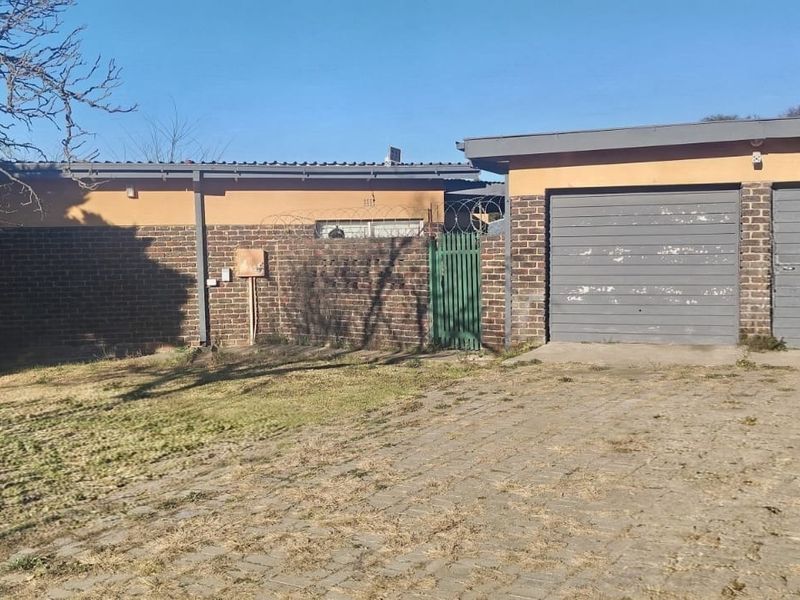 Front exterior view of the property featuring a double garage, brick facade, paved driveway, and security fencing with razor wire.
