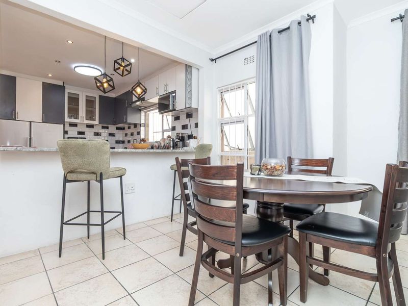 Open plan kitchen and dining area featuring modern cabinetry, a granite breakfast bar, tiled flooring, and contemporary pendant lighting.
