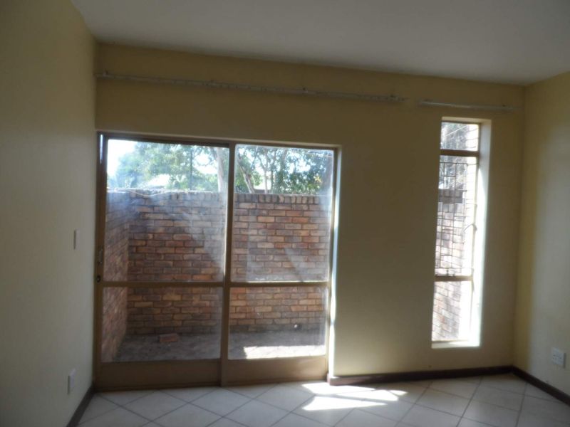 An empty living room featuring tiled flooring, a large sliding glass door, and a window, providing access to a private outdoor area.