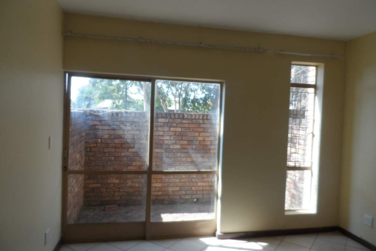 An empty living room featuring tiled flooring, a large sliding glass door, and a window, providing access to a private outdoor area.