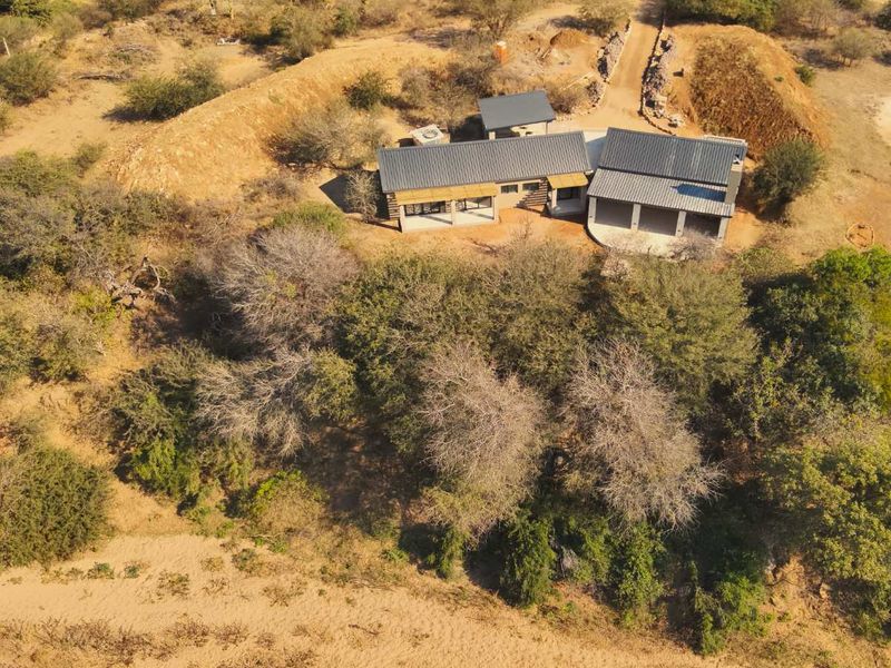 Aerial view of a modern house with a metal roof, covered patio, and surrounding natural landscape.