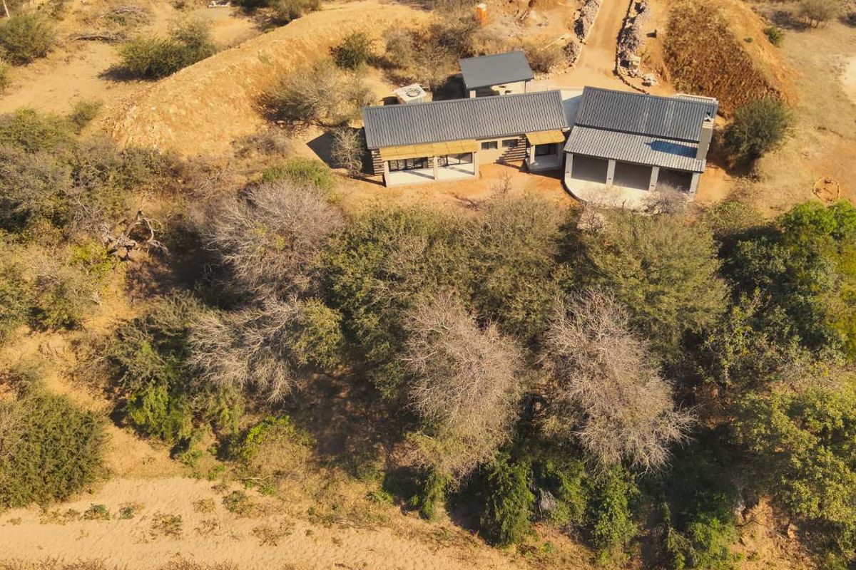 Aerial view of a modern house with a metal roof, covered patio, and surrounding natural landscape.