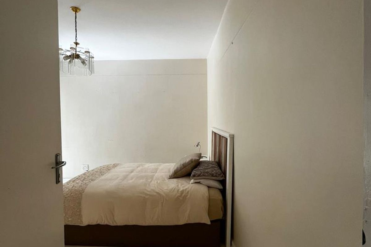 A simple bedroom featuring neutral walls, a classic chandelier, and a functional layout suitable for a comfortable sleeping space.