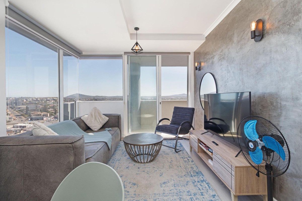 Modern living room featuring a textured feature wall, floor-to-ceiling windows with expansive city views, and direct access to a private balcony.