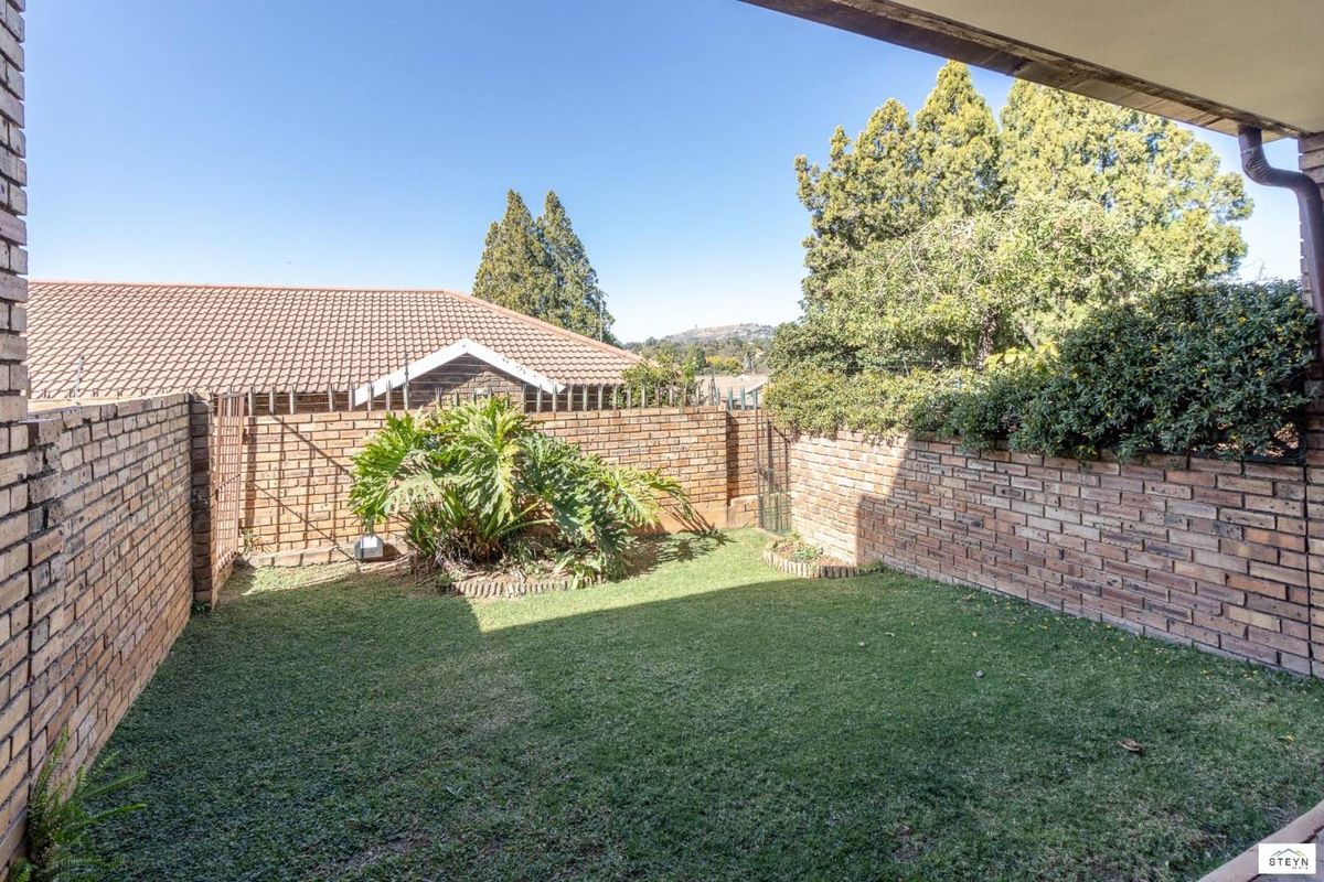 A private rear garden featuring a lawn area enclosed by face brick boundary walls, viewed from a covered patio.