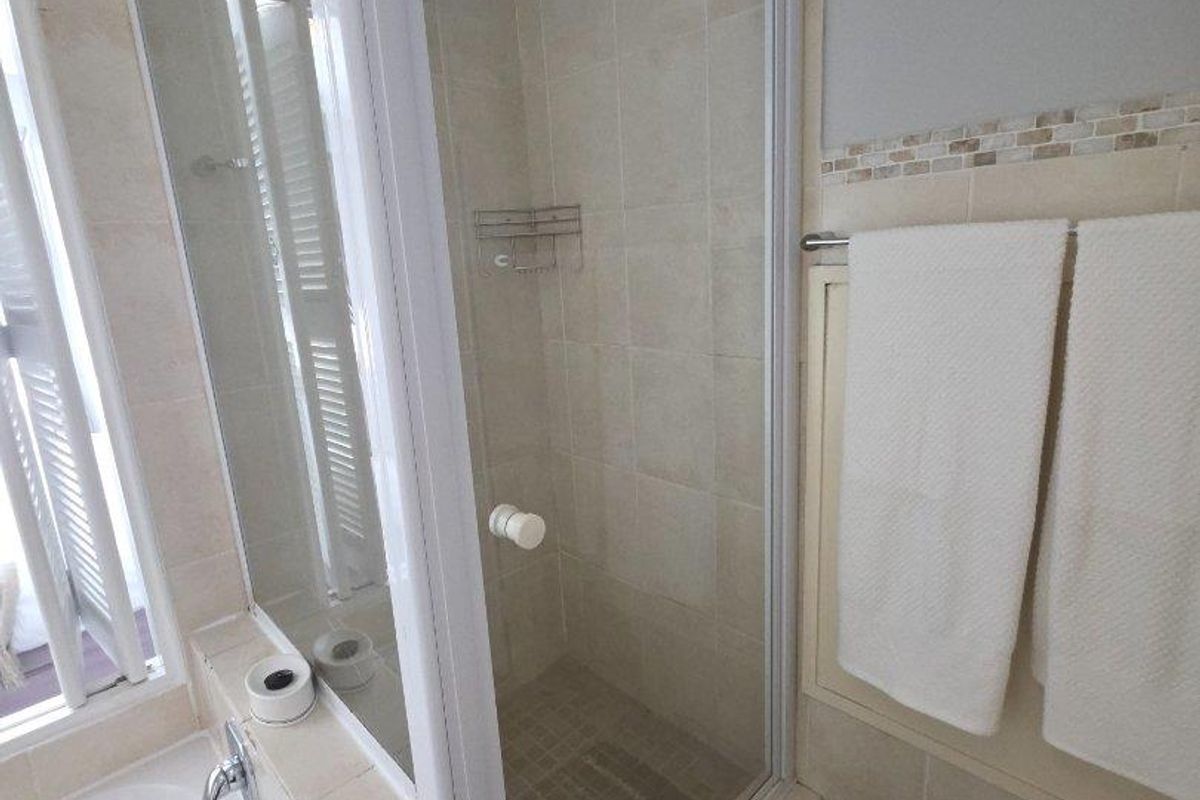 A functional bathroom featuring a glass-enclosed shower cubicle, a built-in bathtub, and neutral wall tiling.