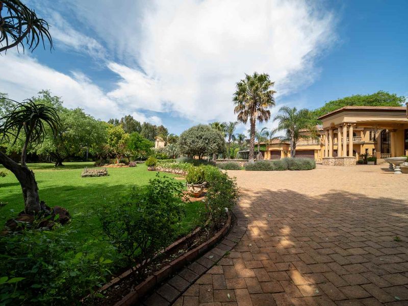 Spacious front exterior featuring a large paved driveway, manicured garden, and an impressive entrance with stone-clad columns.