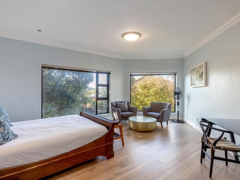 Spacious bedroom featuring large windows with garden views, laminate flooring, and neutral wall tones, offering a bright and comfortable living space.