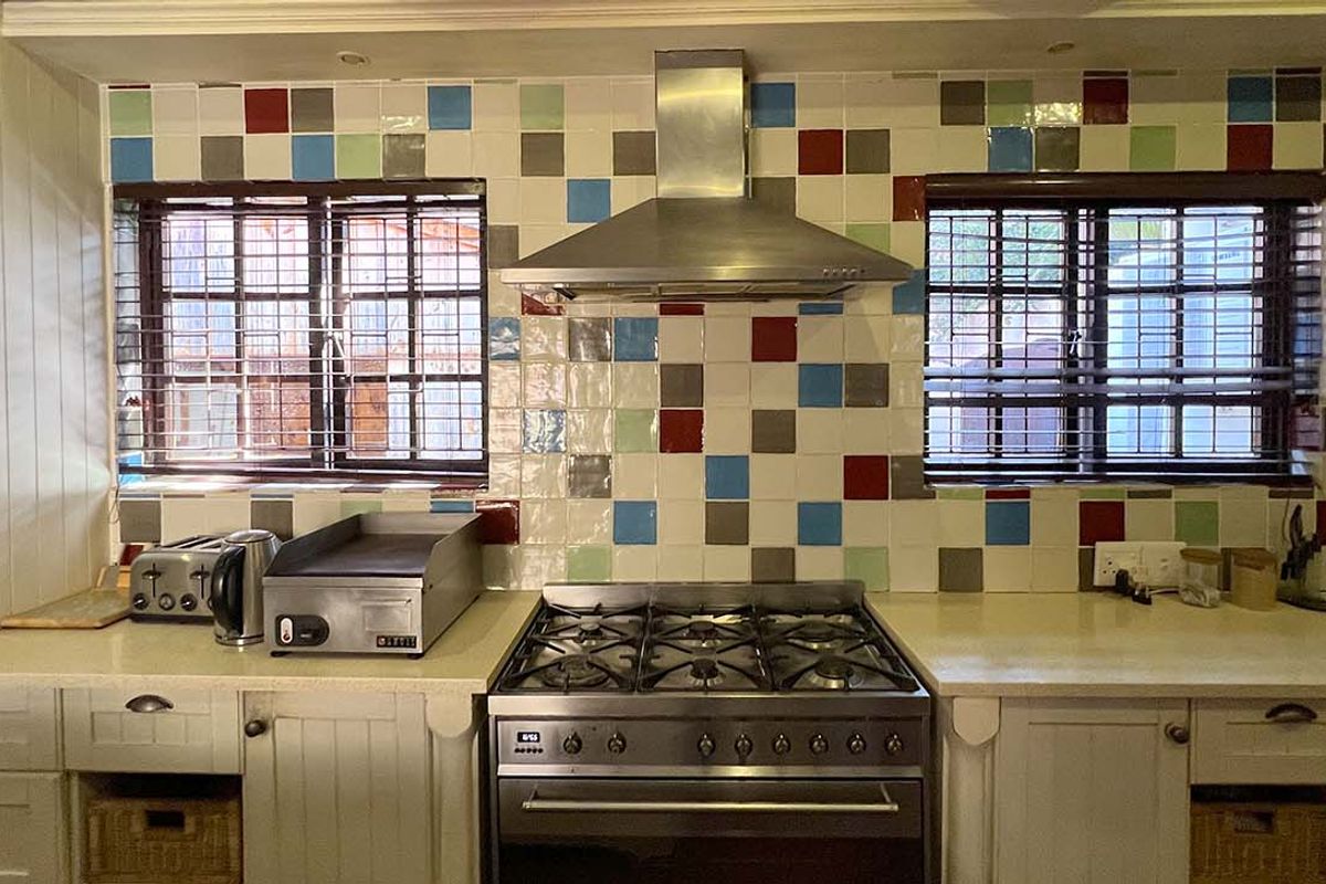 A functional kitchen featuring a stainless steel gas stove, extractor fan, and multi-colored tiled backsplash with ample counter space and cabinetry.