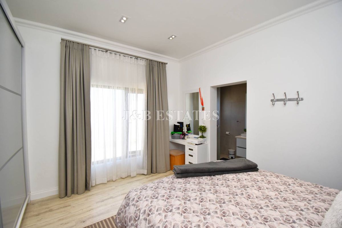 A well-maintained bedroom featuring recessed ceiling lighting, crown molding, light wood-look flooring, and an en-suite bathroom entrance.
