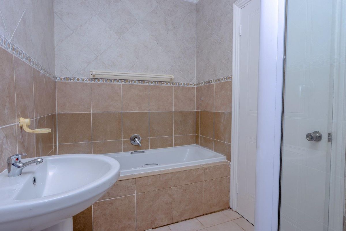 A functional bathroom featuring a pedestal washbasin, a built-in bathtub, and a separate shower enclosure with neutral ceramic wall and floor tiling.