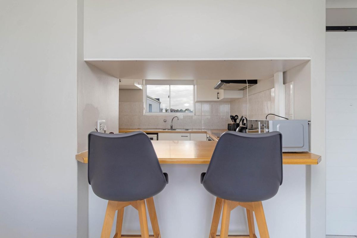 A functional kitchen featuring a breakfast bar, tiled backsplash, stainless steel sink, and built-in cabinetry, viewed from the adjacent living area.