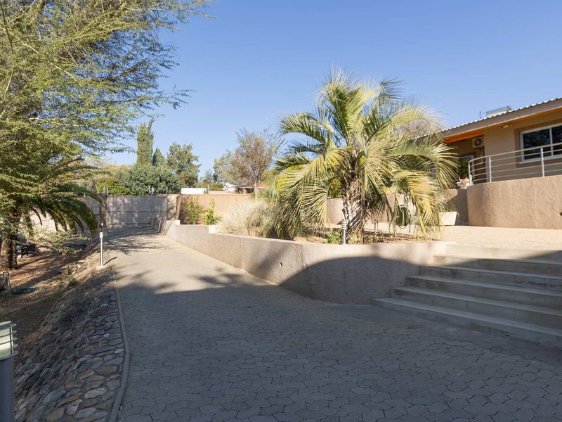 Front exterior view featuring a paved driveway, concrete stairs with metal railings, and a landscaped retaining wall area.