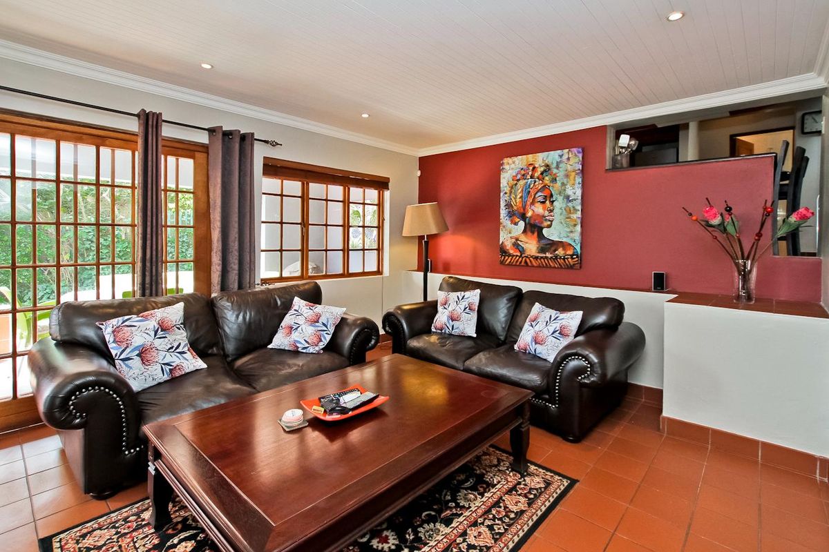 A cozy living room featuring terracotta floor tiles, timber-framed glass doors leading to the patio, and a distinctive red accent wall.
