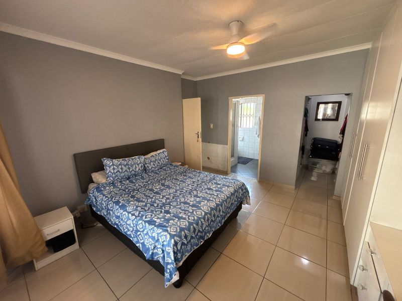 Spacious bedroom featuring tiled flooring, built-in cupboards, a ceiling fan, and direct access to an en-suite bathroom.
