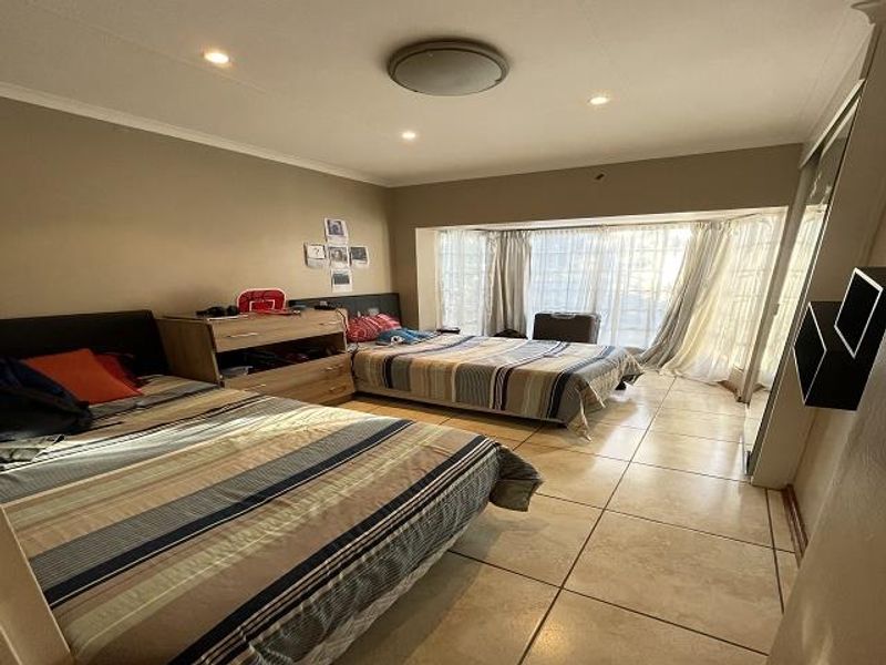 Spacious bedroom featuring large bay windows, tiled flooring, and recessed lighting, offering a bright and functional living space.