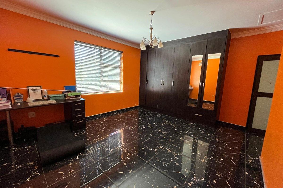 A bedroom featuring dark built-in wardrobes with mirrored panels, black marble-effect floor tiles, and bright orange walls.