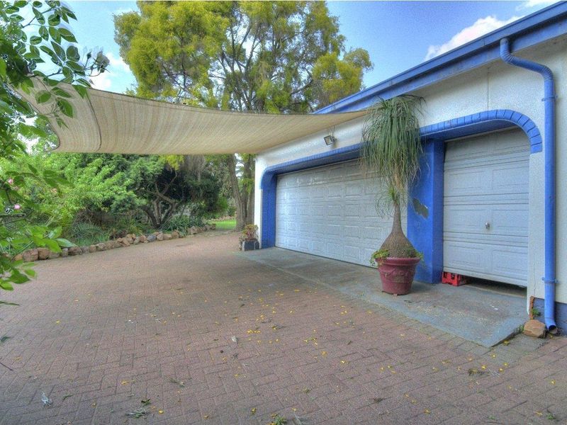 Exterior view of a multi-car garage with a paved driveway and overhead shade sail, showing visible wear to the building facade.