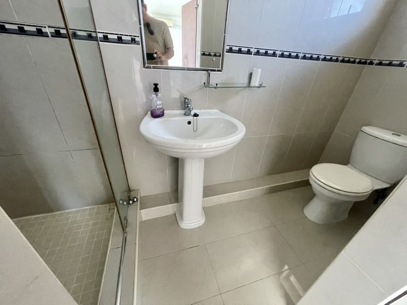 A functional bathroom featuring a pedestal basin, toilet, and a glass-enclosed shower with neutral wall and floor tiling.