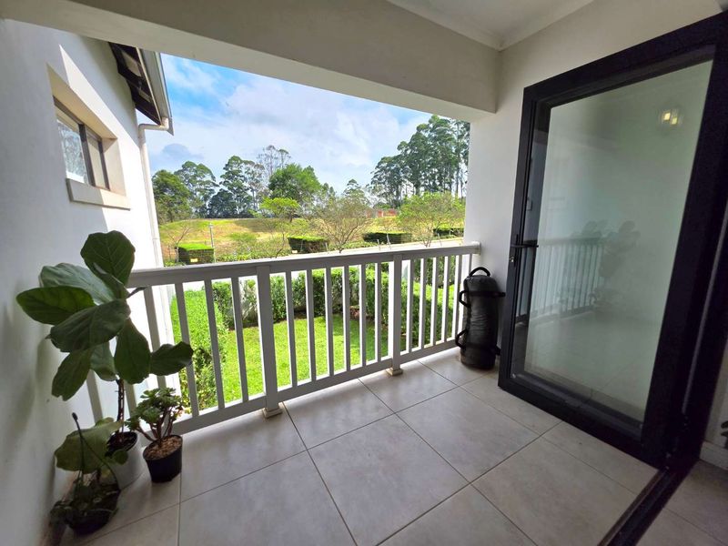 A clean, covered balcony featuring tiled flooring, a white balustrade, and a large sliding glass door providing access to the interior.