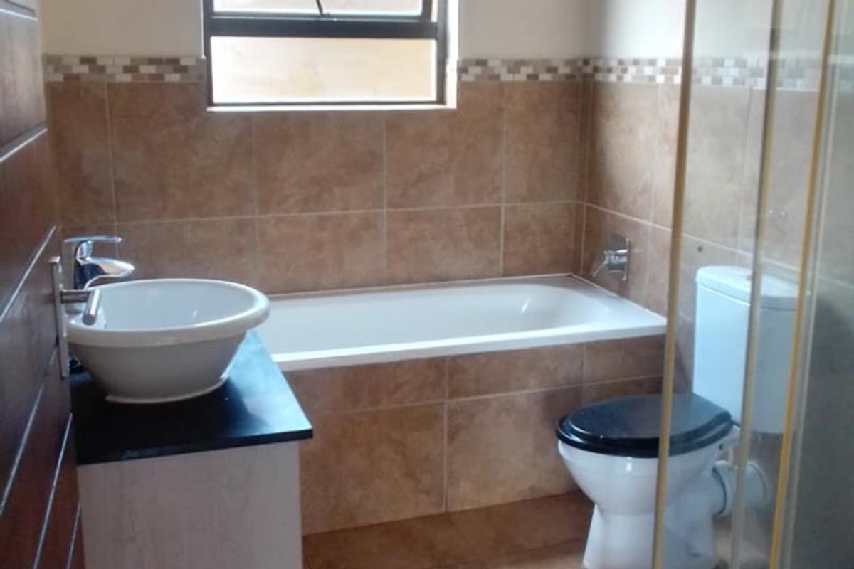 A functional bathroom featuring a built-in bathtub, a separate glass-enclosed shower, a vanity with a basin, and a toilet with tiled walls and flooring.