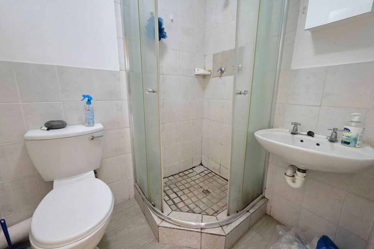 A functional bathroom featuring a corner shower enclosure, wall-mounted basin, and standard toilet with tiled walls and flooring.