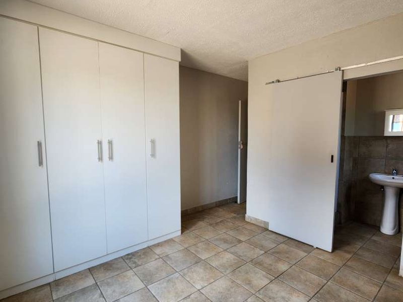 A spacious bedroom featuring neutral tiled flooring, ample built-in cupboard storage, and direct access to an en-suite bathroom.