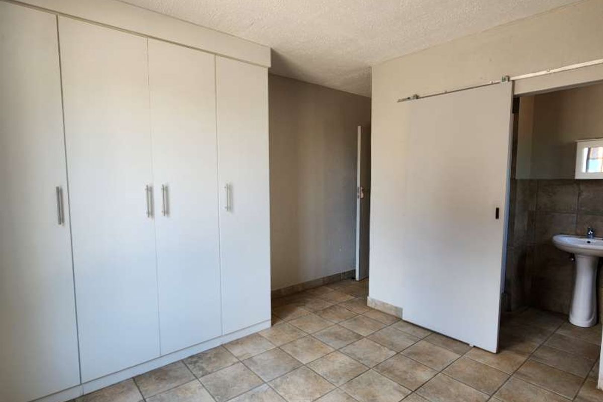 A spacious bedroom featuring neutral tiled flooring, ample built-in cupboard storage, and direct access to an en-suite bathroom.