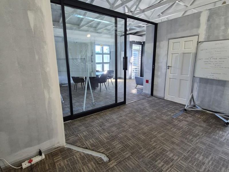 An office space featuring exposed roof trusses, a modern glass partition, and carpet tile flooring, currently in an unfinished state requiring cosmetic completion.