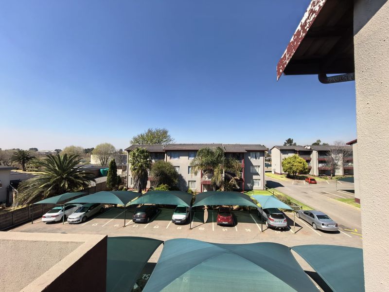View of the apartment complex parking area featuring multiple shade cloth carports and paved parking bays.